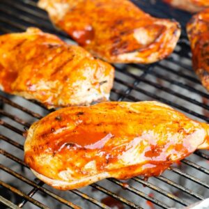 Jalapeno Popper stuffed barbecue chicken breasts slathered with sauce on a grill.