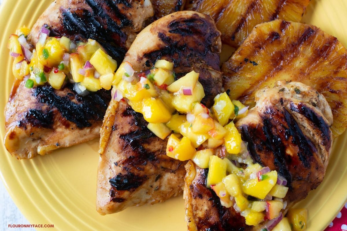 Three grilled chicken breasts with grilled pineapple slices served with peach mango salsa.