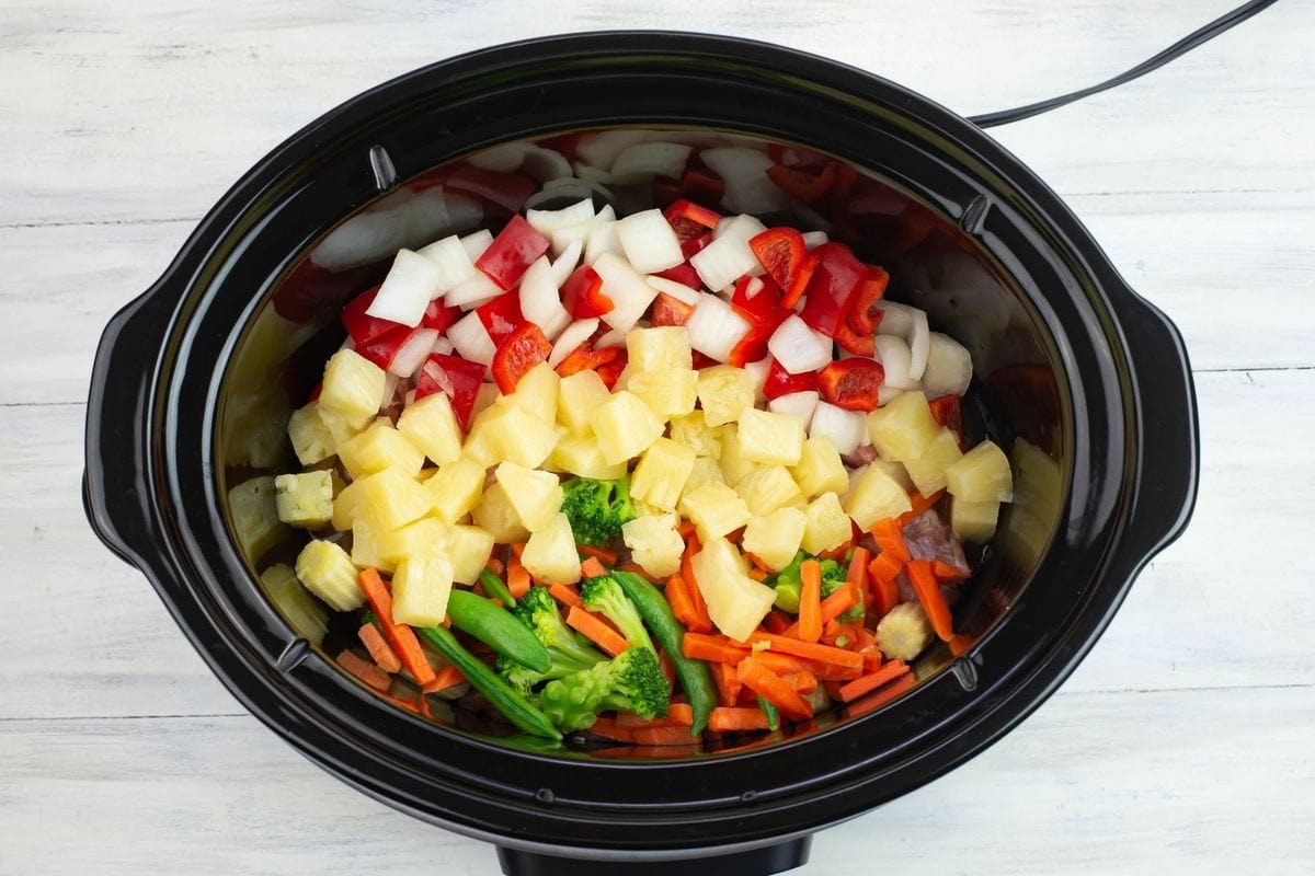 Pineapple chunks, cubed pork and vegetables in a large crock pot before slow cooking.