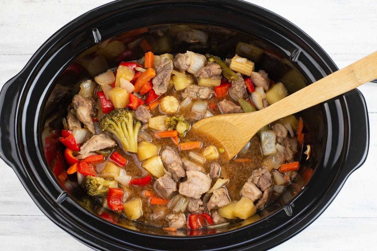 A slow cooker filled with cooked pork and vegetables before adding a thickener.