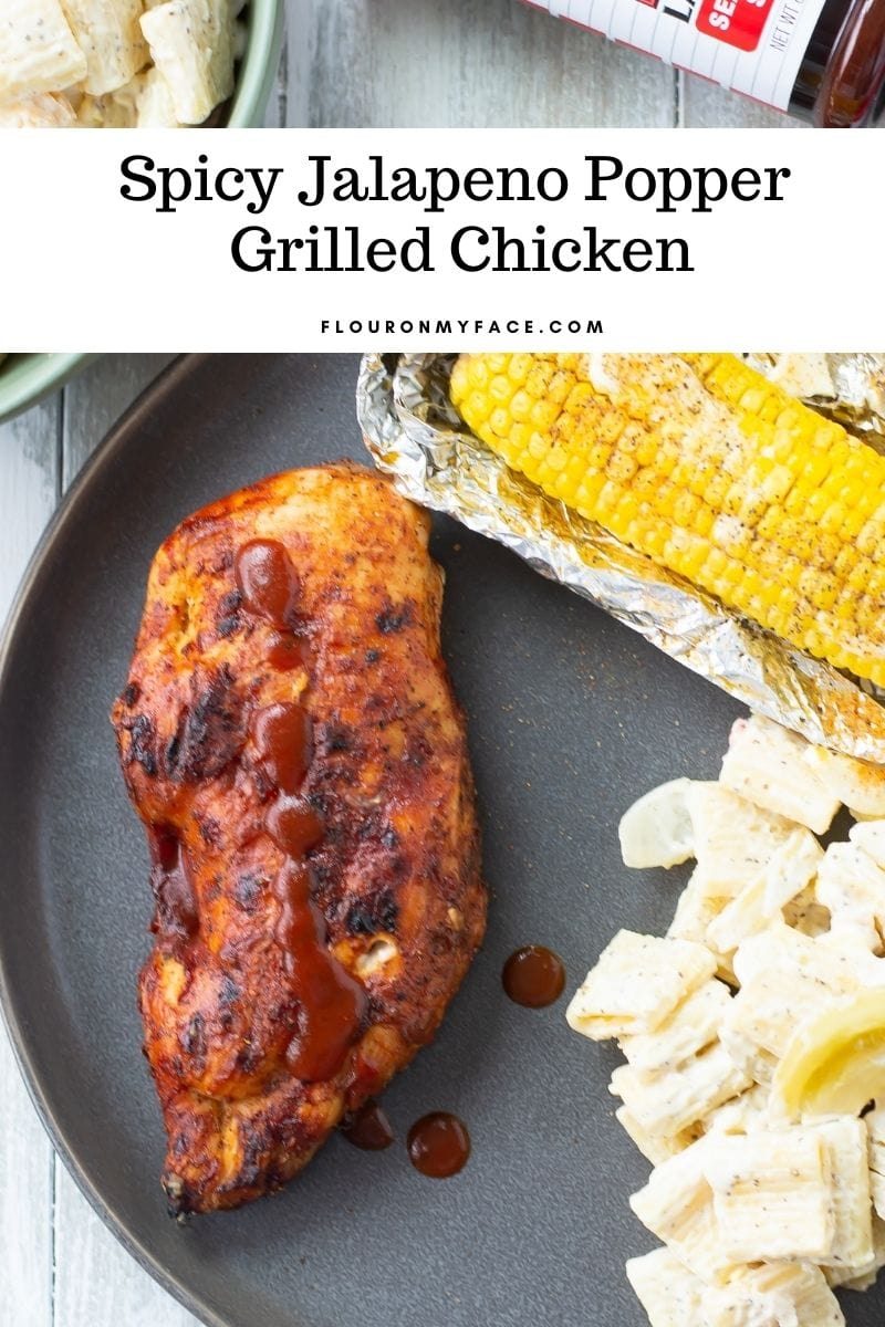 A black plate with Spicy Jalapeno Popper Grilled Chicken breast, grilled corn on the con and Pickled Tomato Pasta Salad