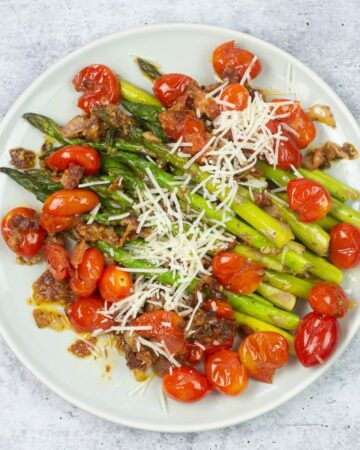 Sautéed asparagus with tomatoes and bacon on a plate.