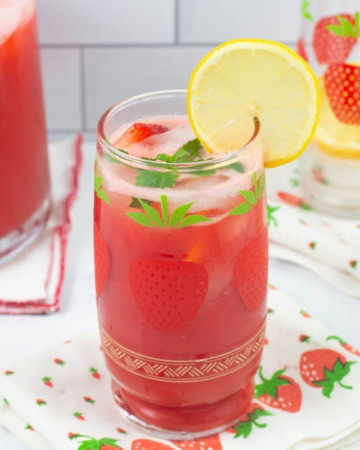 Decorative glass filled with ice, strawberry lemonade and garnished with lemon slice and mint sprig.
