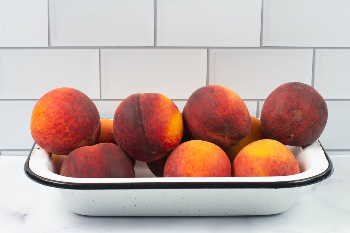Washed ripe peaches stacked in a small enamel bowl.