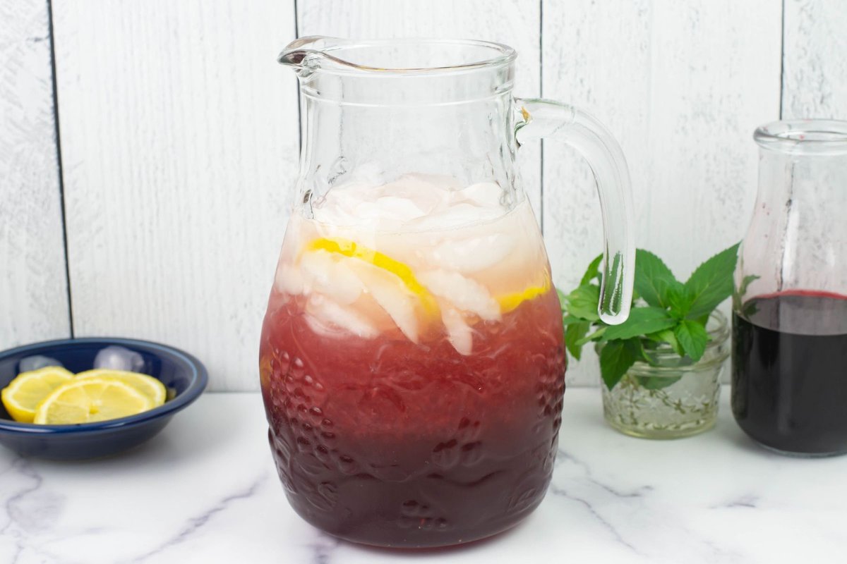 Glass pitcher filled ¾ with ice cubes and a hibiscus lemonade mocktail.