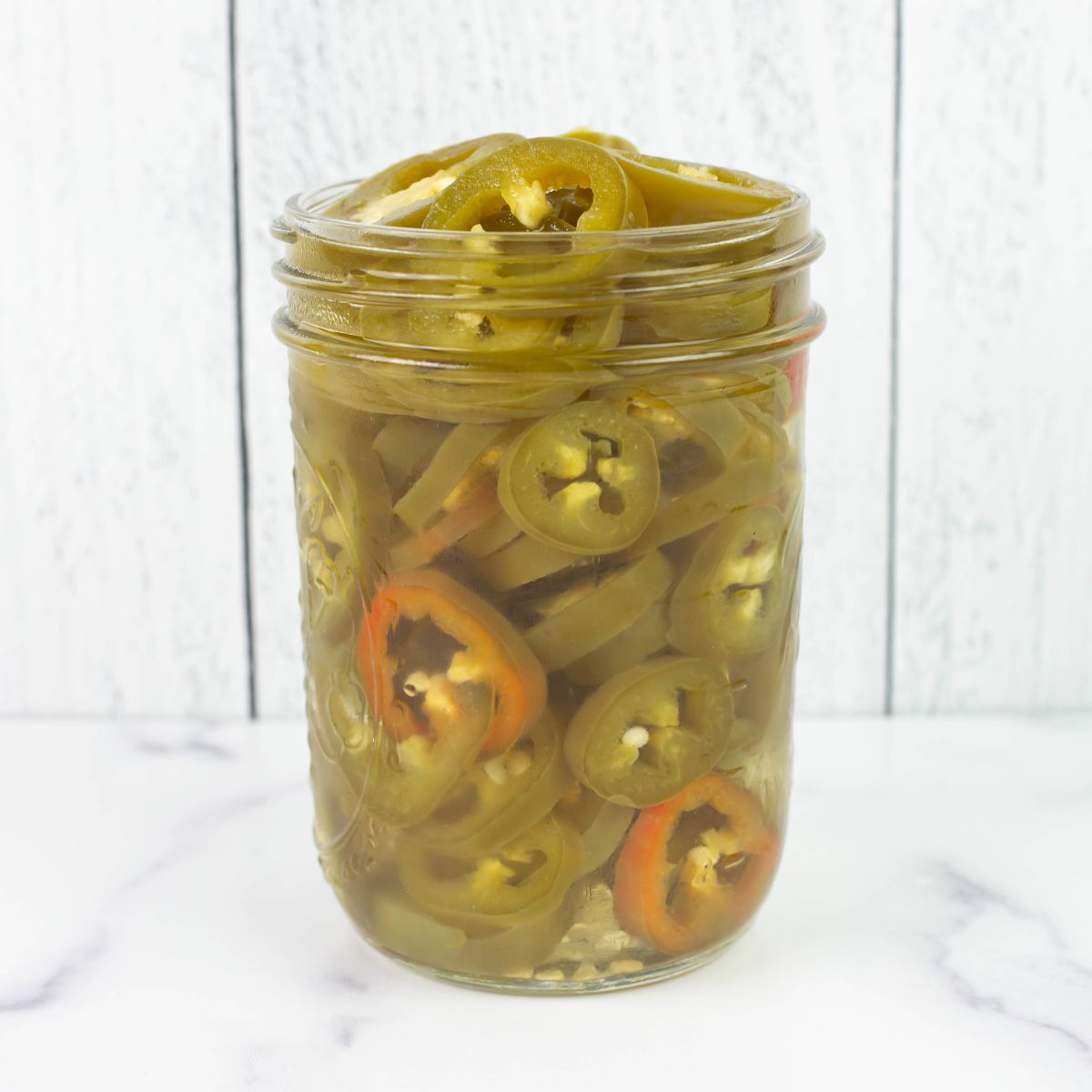 A canning jar filled with pickled pepper slices.