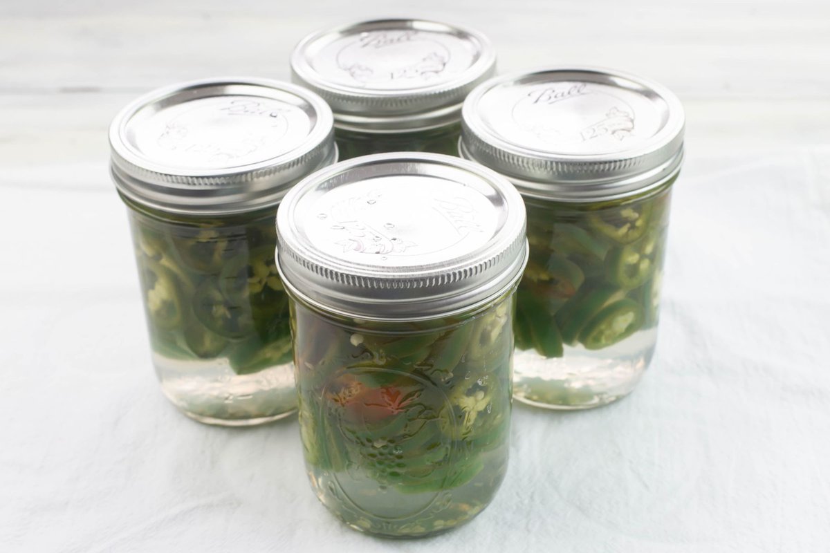 Canning jars filled with sliced jalapeno peppers and a brine.