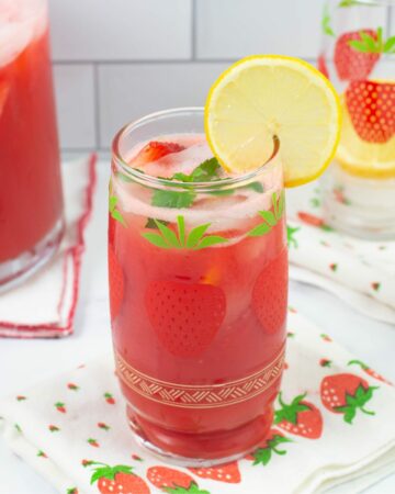 Decorative glass filled with ice, strawberry lemonade and garnished with lemon slice and mint sprig.