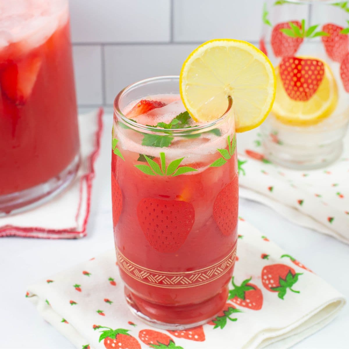 Decorative glass filled with ice, strawberry lemonade and garnished with lemon slice and mint sprig.