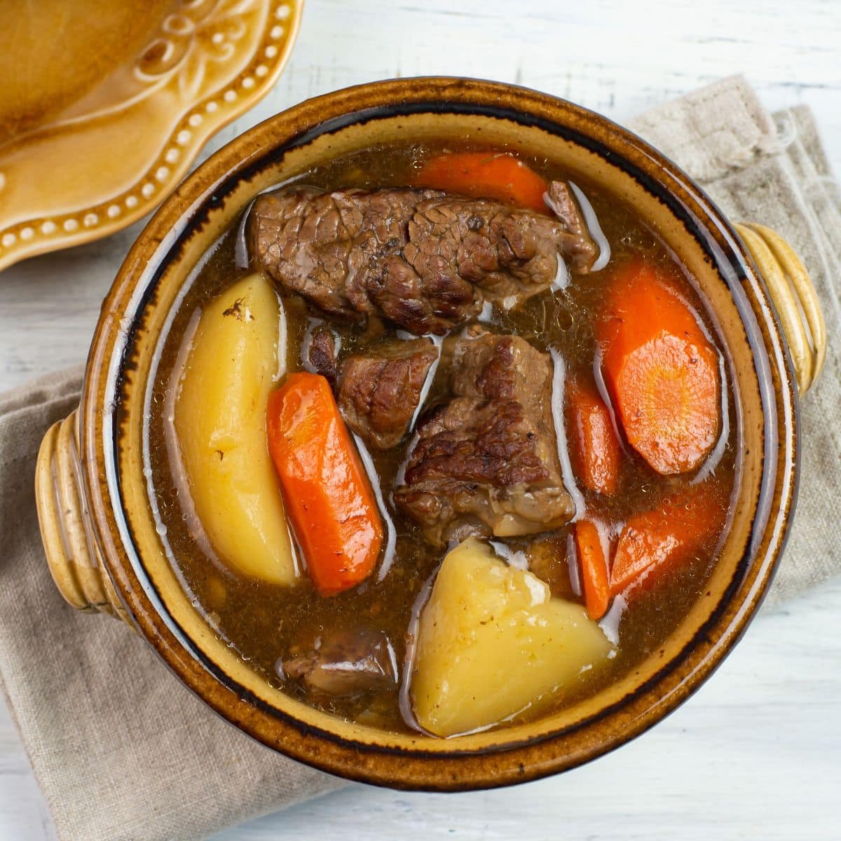 Beef stew with chunky vegetables in a brown serving crock.