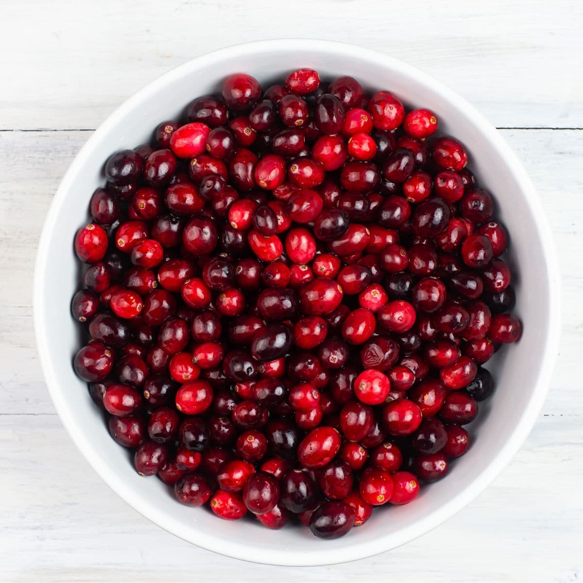 A white glass bowl filled with fresh cranberries.