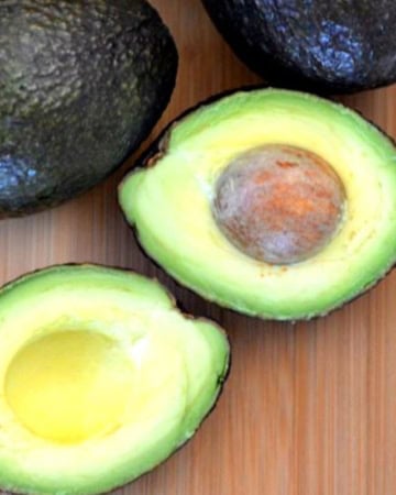 Fresh cut and uncut avocados on a wooden cutting board.