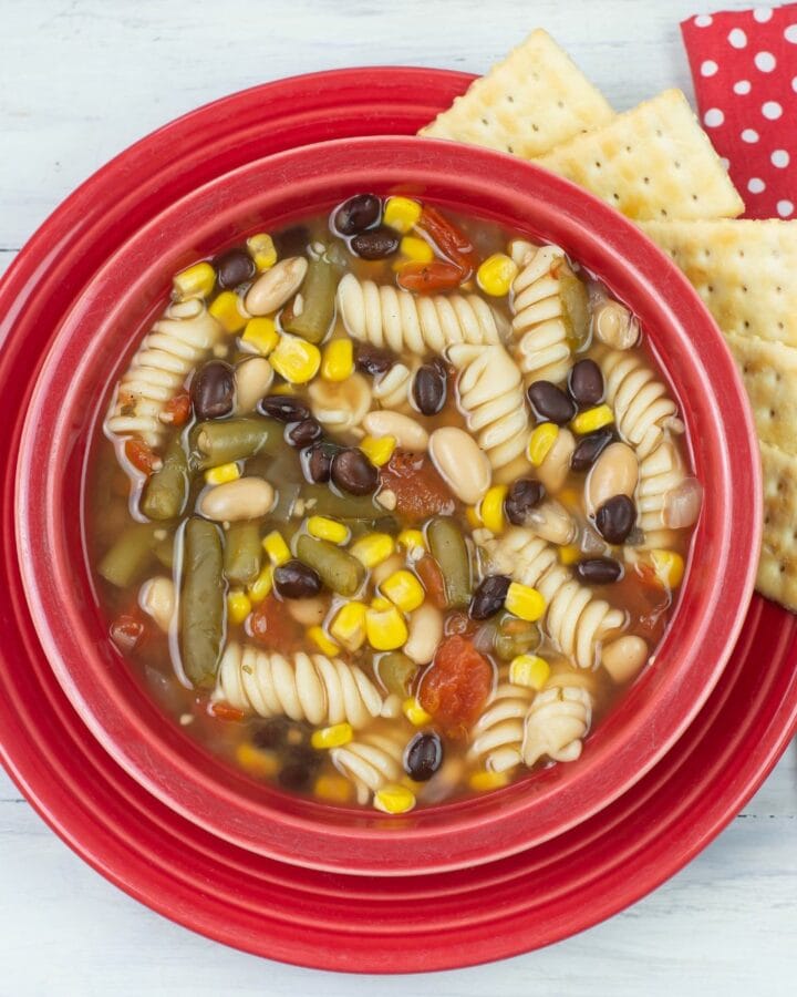 Vegetable Pasta Soup in a red bowl with crackers on the side.