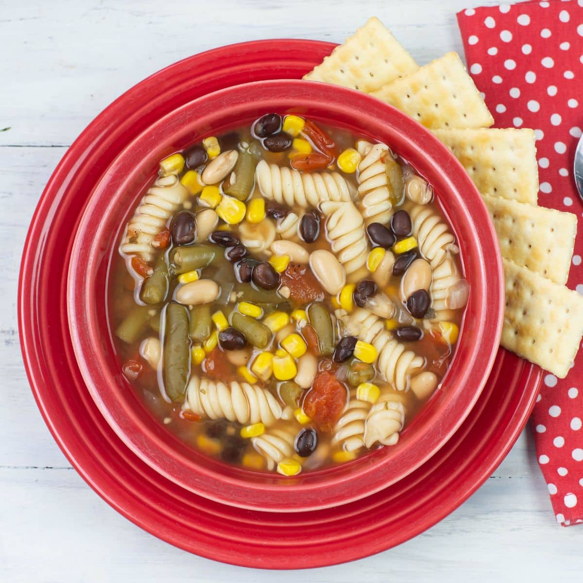 Vegetable Pasta Soup in a red bowl with crackers on the side.