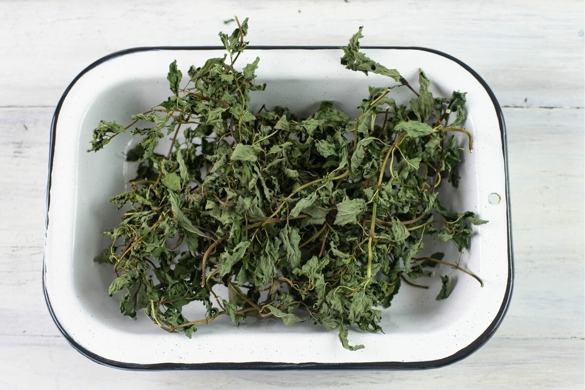 Dried mint leaves and stems in a square metal bowl.