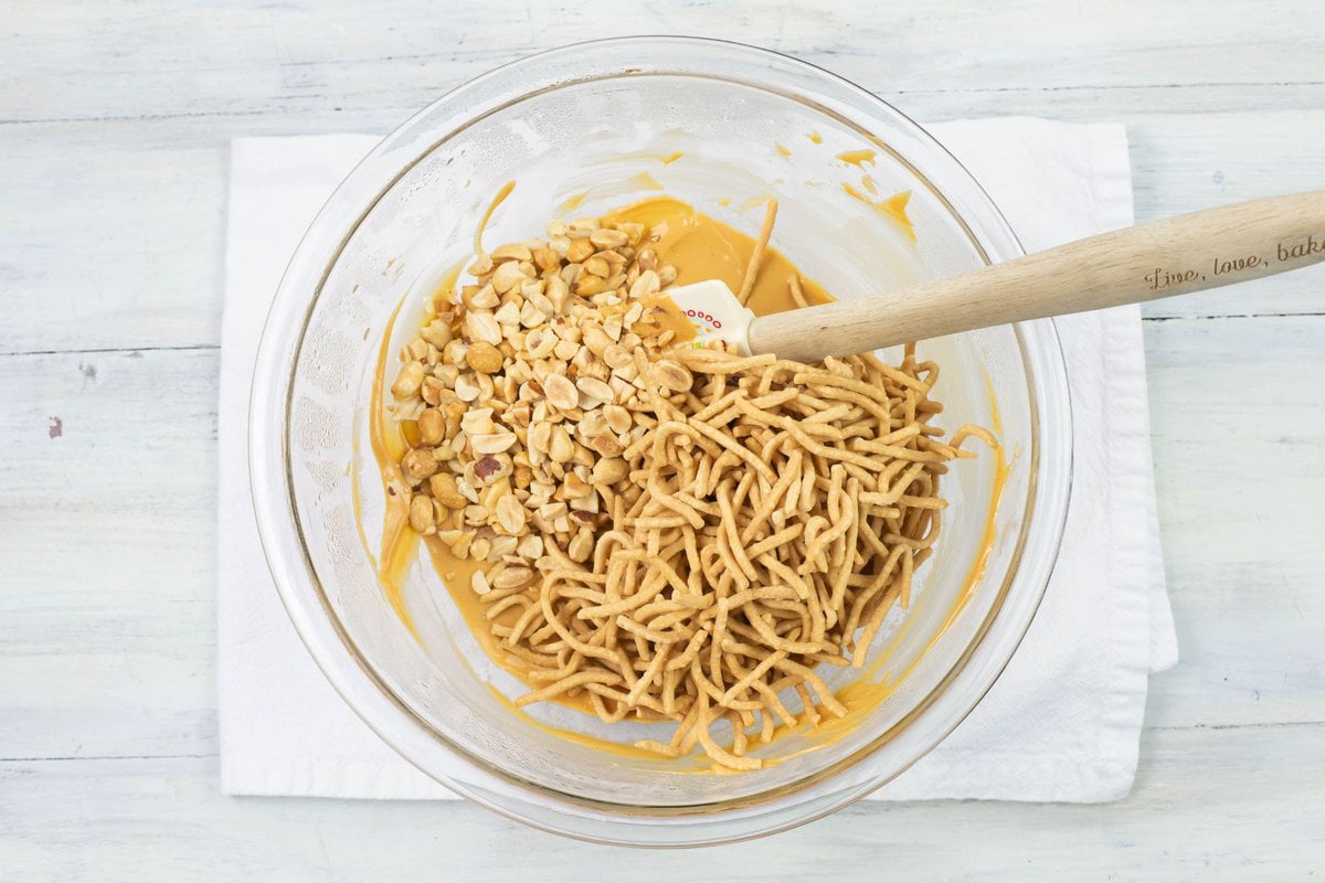 Tossing and coating the crunchy noodles and crushed peanuts in a bowl.