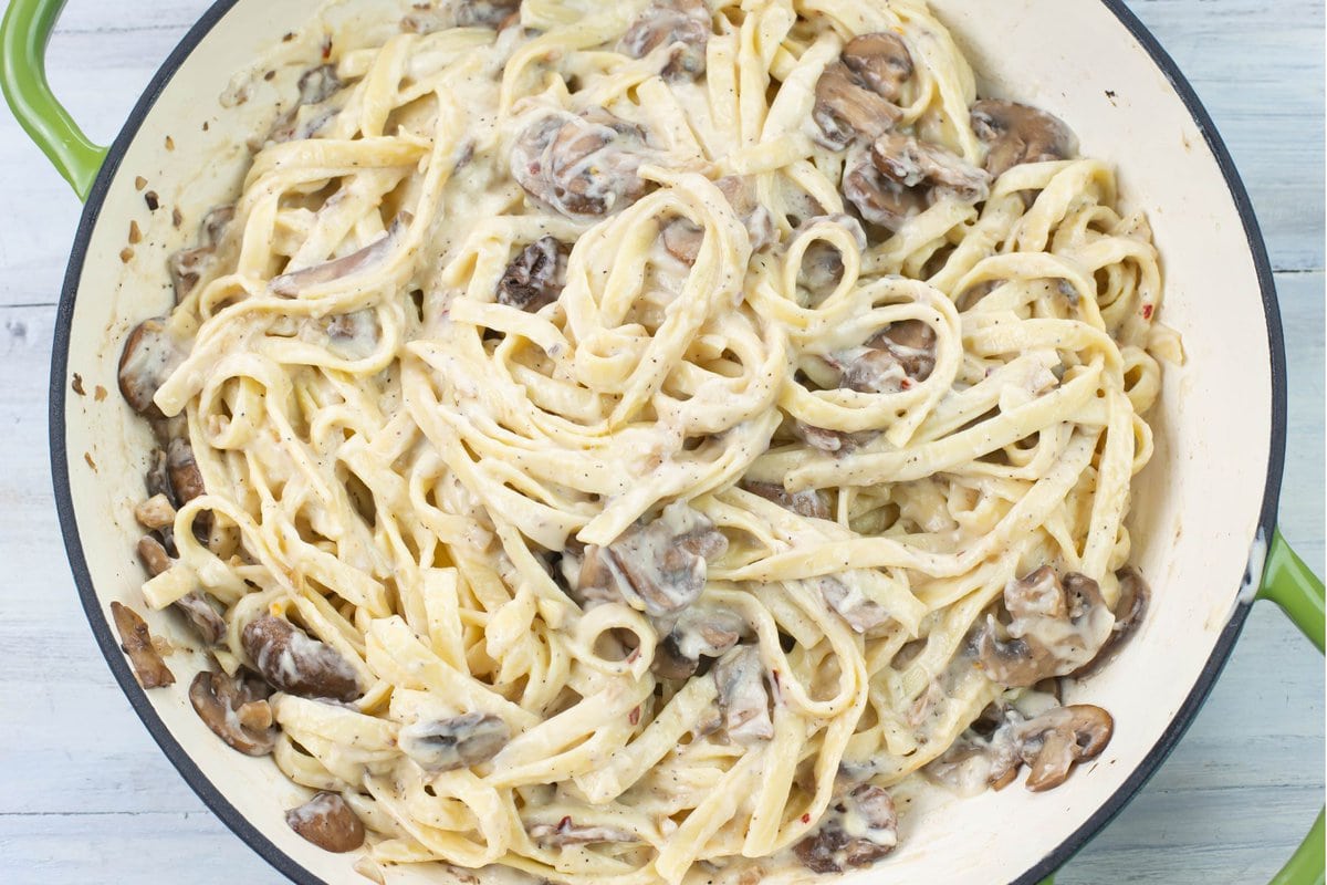 Closeup image of a skillet filled with creamy mushroom alfredo sauce with fettucine noodles.