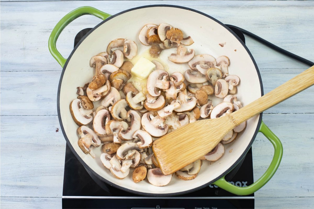 sautéing mushrooms with butter in a green enamel skillet.
