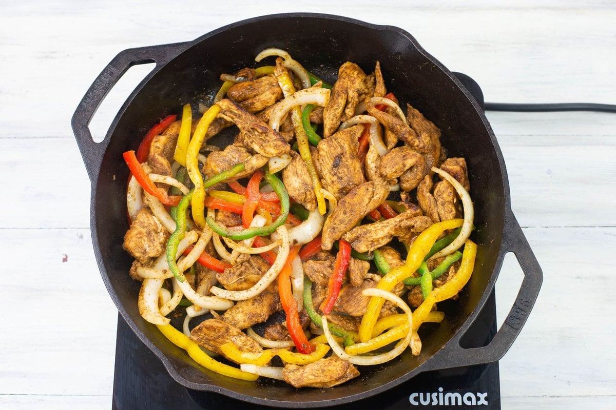 Cooked chicken, bell peppers, and onions in a iron skillet.