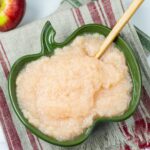 Homemade apple sauce in a green apple shaped serving bowl on a linen towel.