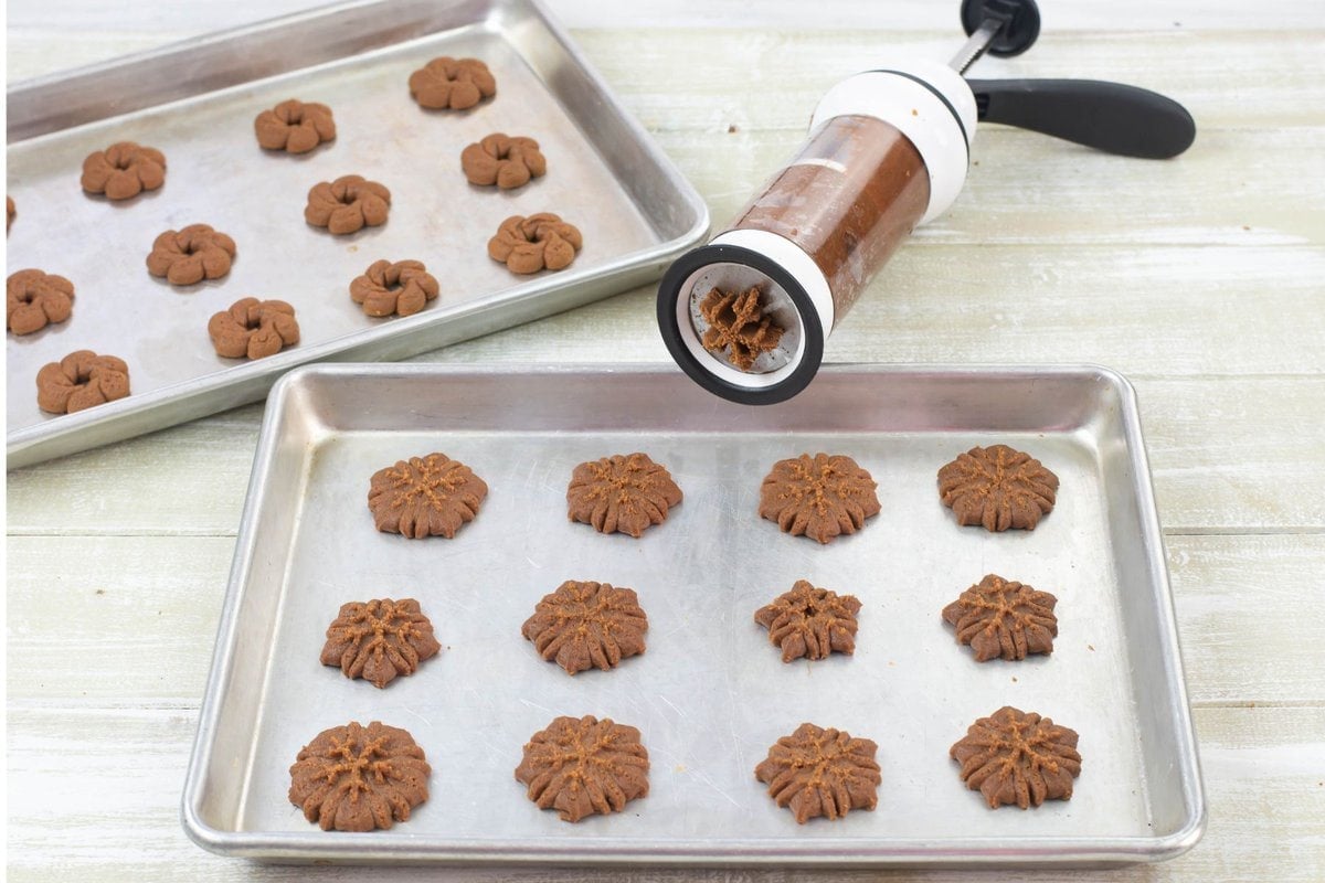 Cookie press with a snowflake disk attached and a cookie sheet with the cookies pressed.