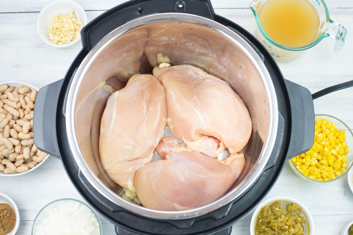 Three skinless boneless chicken breast arranged on the bottom of the Instant Pot insert.