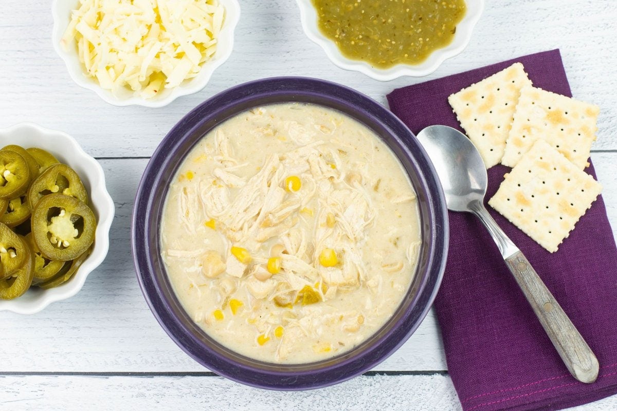 A bowl of creamy cheesy white chicken chili with toppings and crackers.