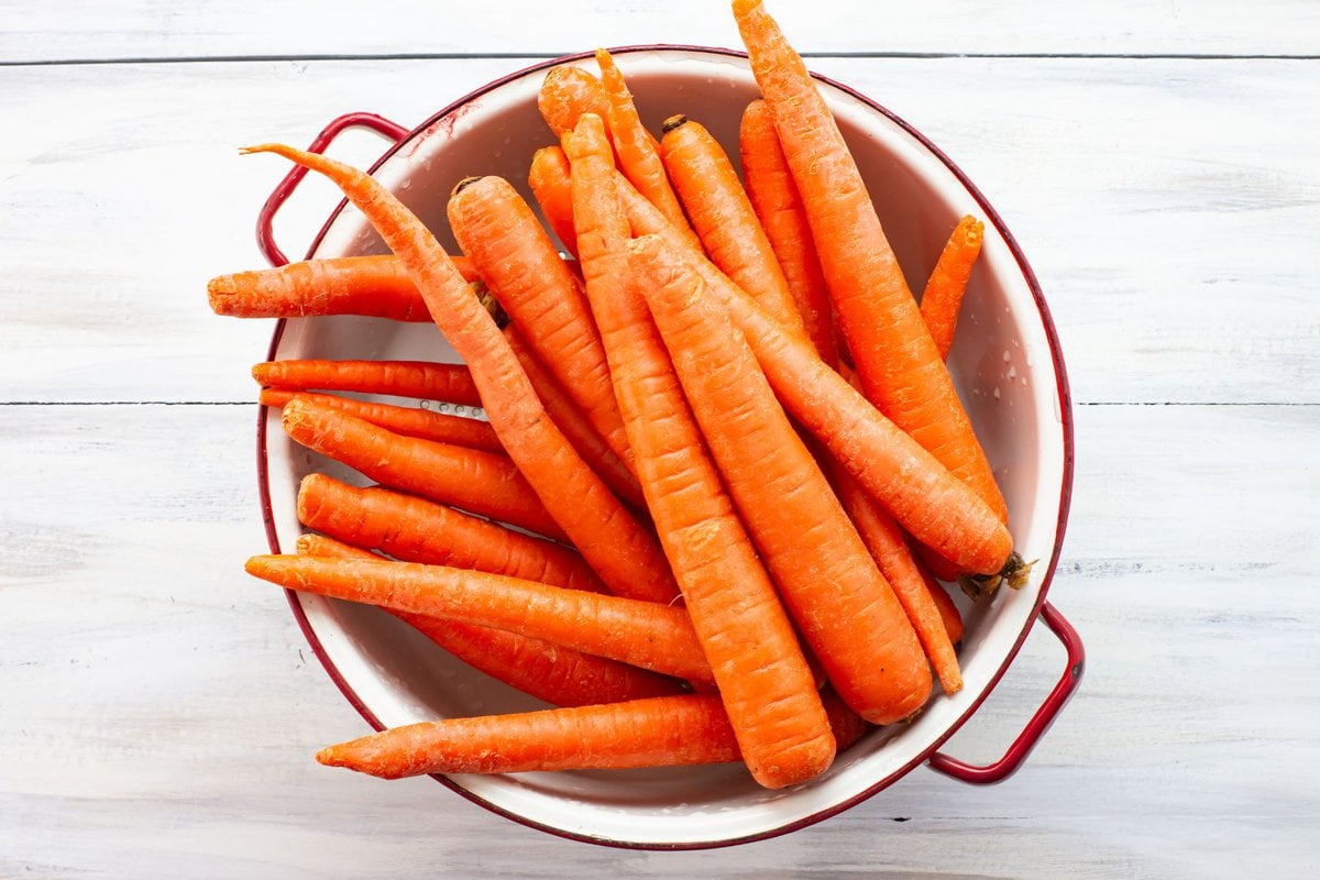 Fresh whole carrots in a white enamel colander.