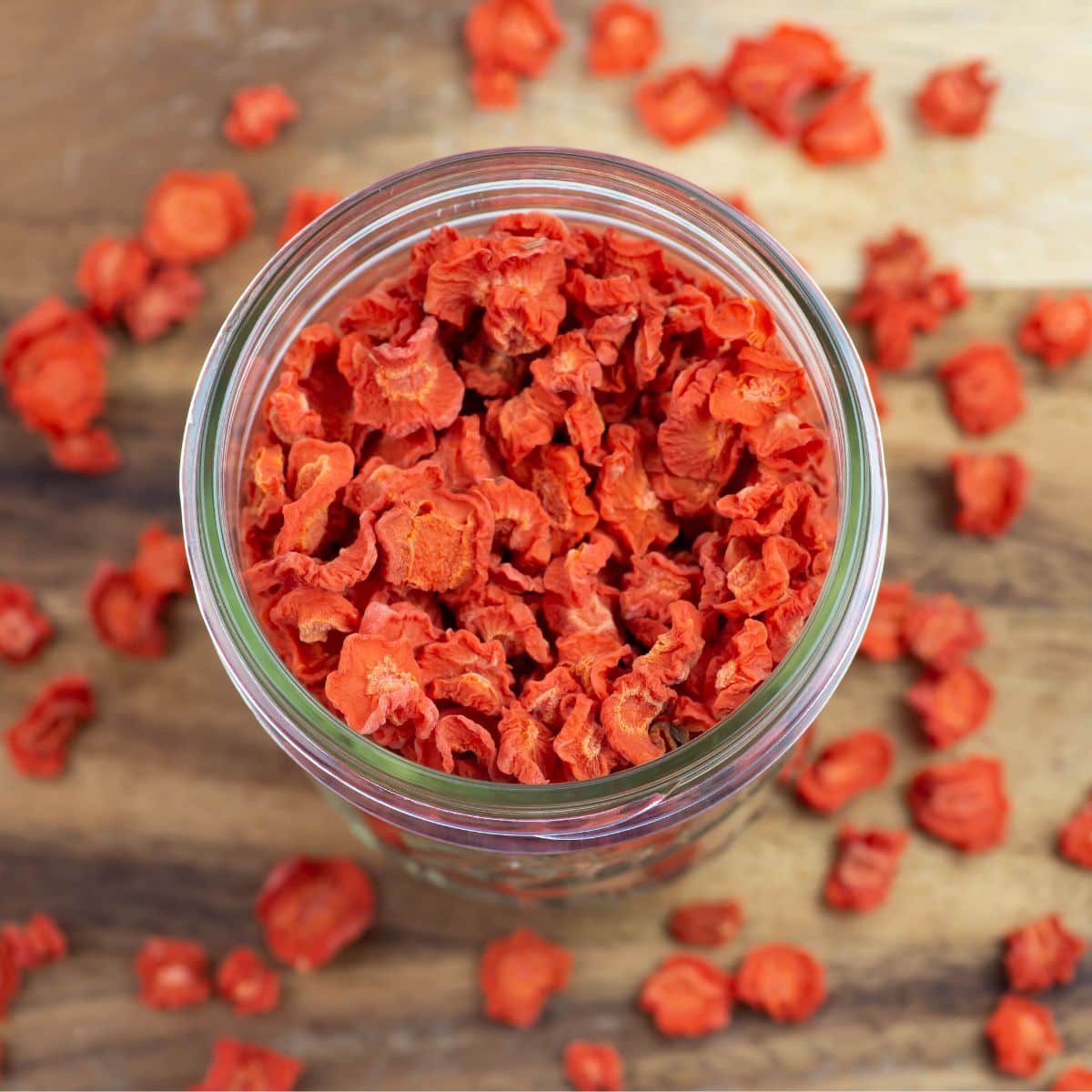 Overhead image of dehydrated carrots in a glass mason jar with some scattered on a cutting board.