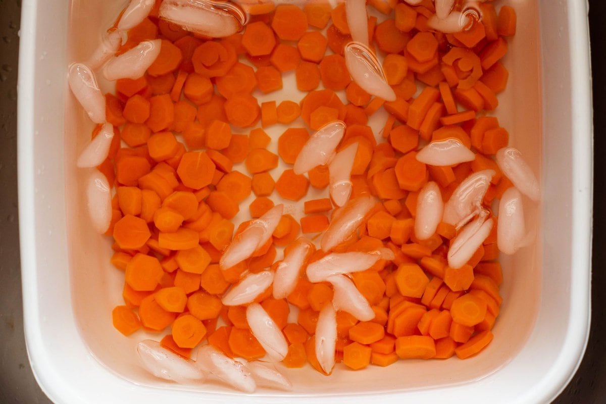 A plastic tub filled with an ice bath to cool the blanched carrots quickly.