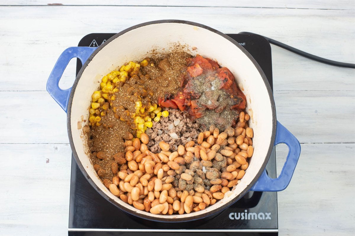 Adding taco seasonings to the soup ingredients in a Dutch oven on a burner.