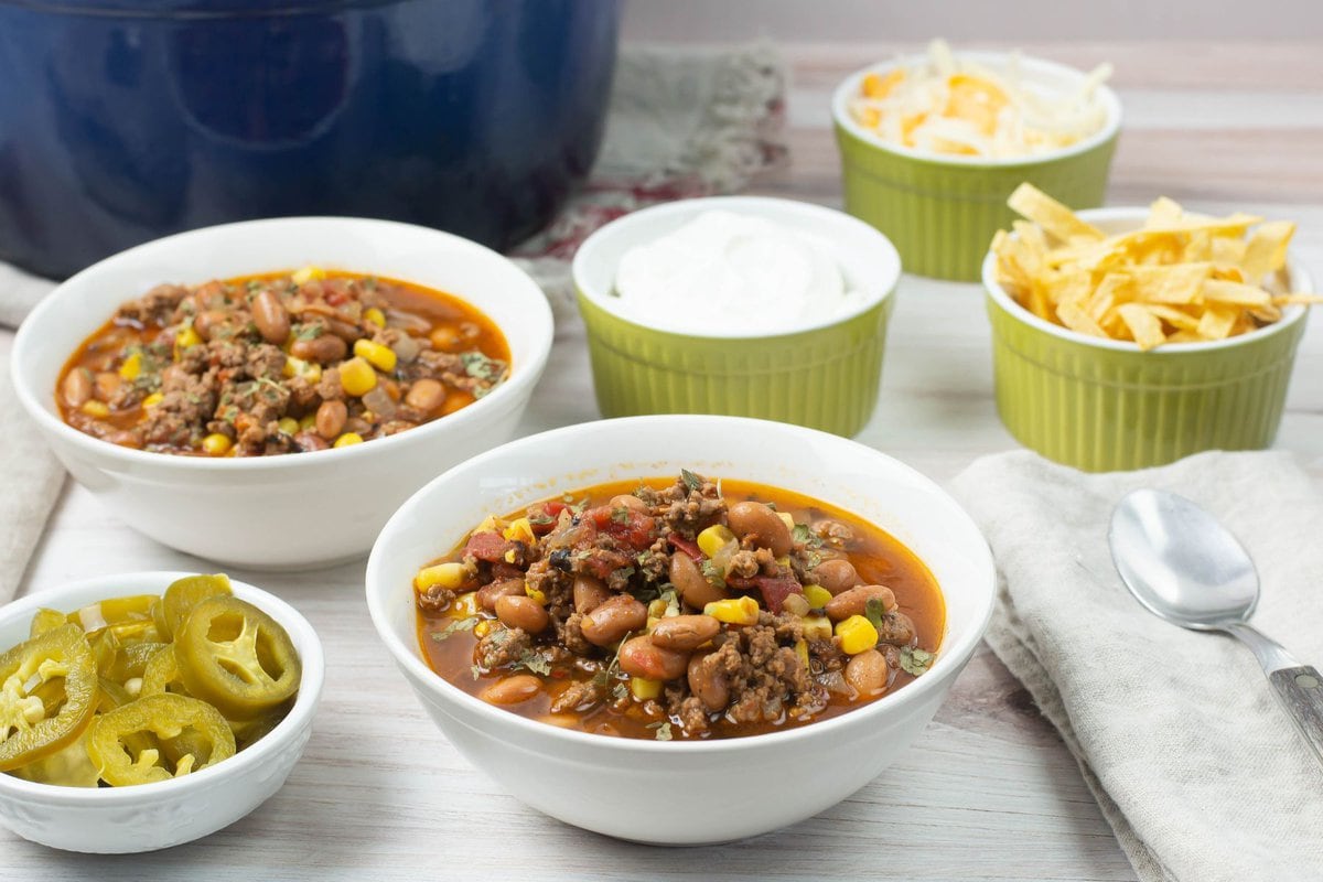Taco soup in a bowl with small bowl of cheese, jalapenos, and chips.