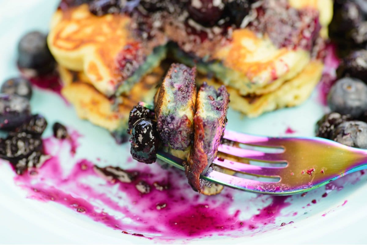 A closeup of a fork with a bite of pancakes served with blueberry sauce.