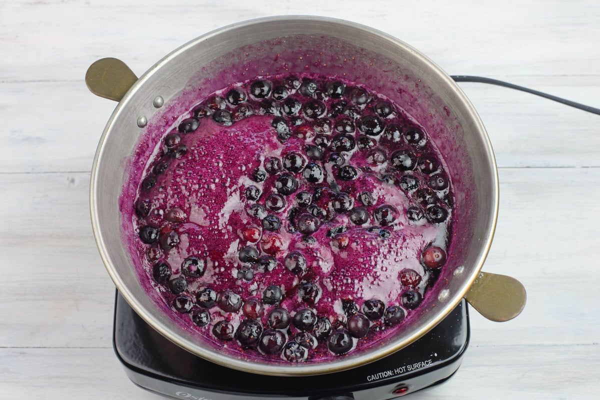 The blueberries start to simmer in the pan.