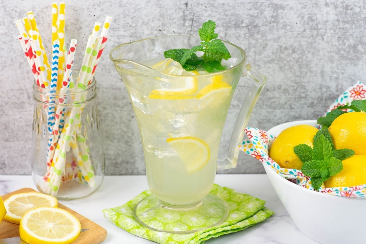 A glass pitcher filled with homemade lemonade, lemon slices and a sprig of mint.
