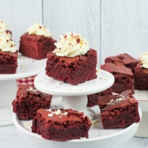Red Velvet Brownies topped with cream cheese frosting with white chocolate curls on cake stands.