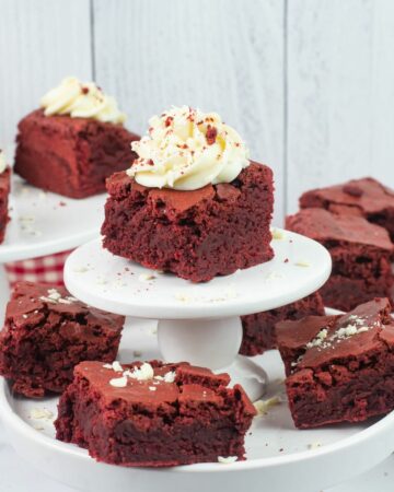 Red Velvet Brownies topped with cream cheese frosting with white chocolate curls on cake stands.