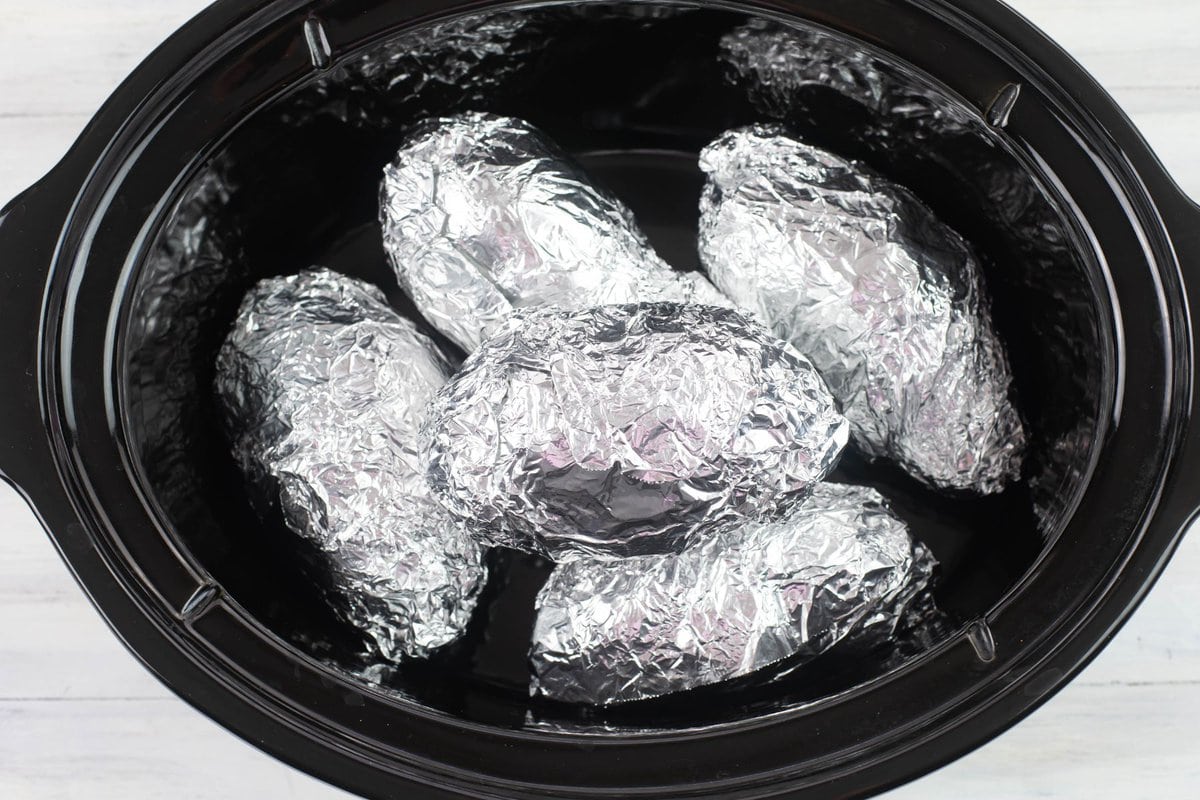 Foil wrapped sweet potatoes stacked in a 8 quart crock pot.