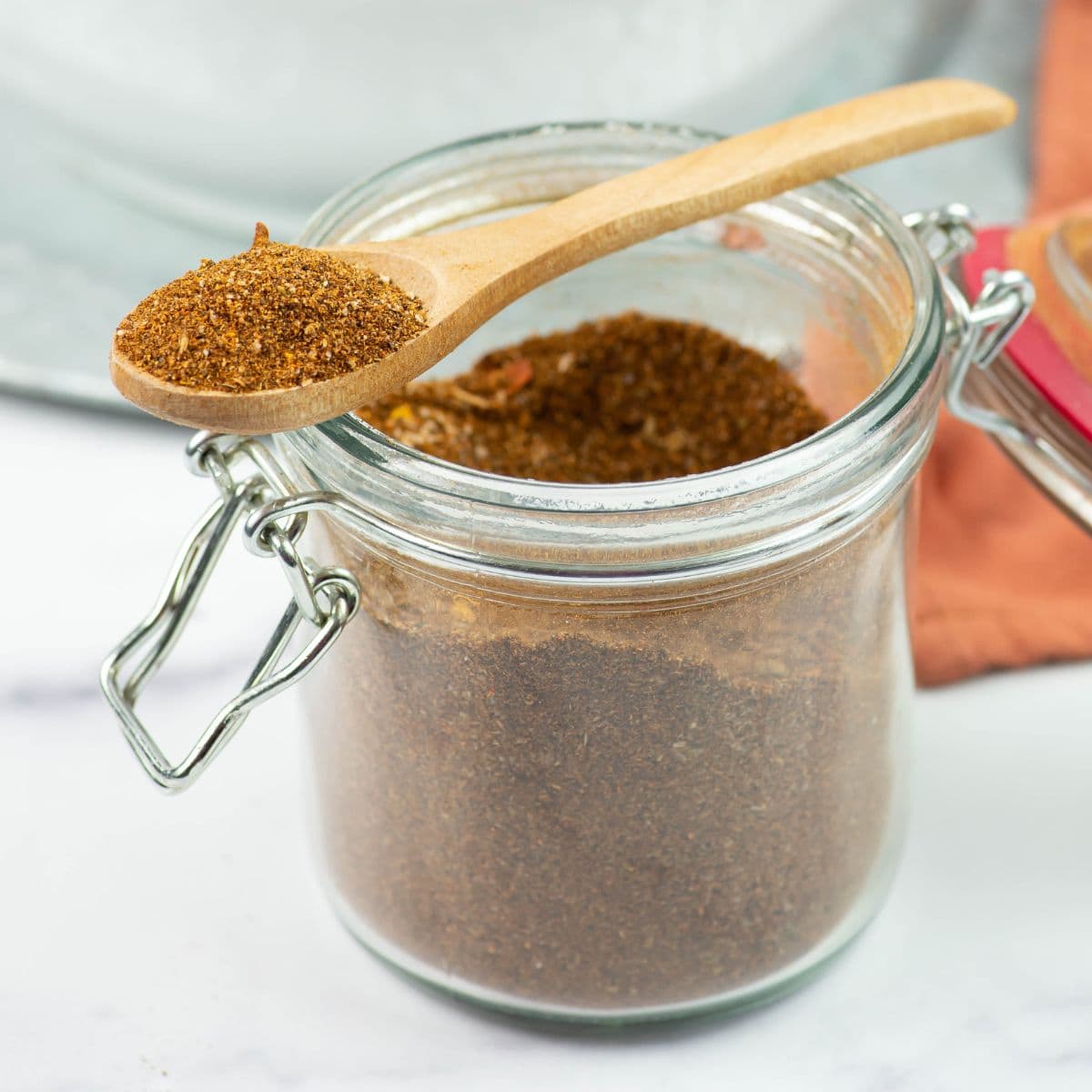 Gourmet Taco Seasoning in a glass jar with a scoop full on a wooden spoon.