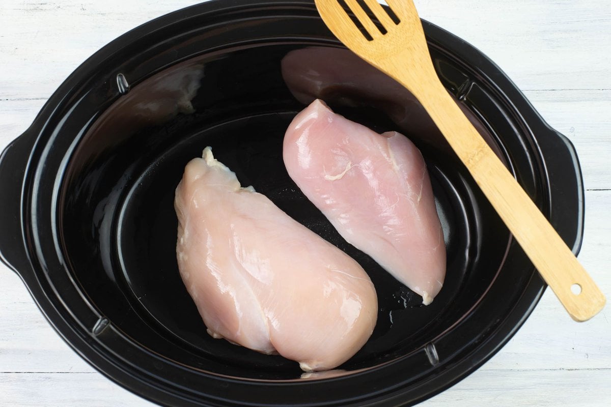 Two pieces of boneless chicken on the bottom of the crock pot crock.