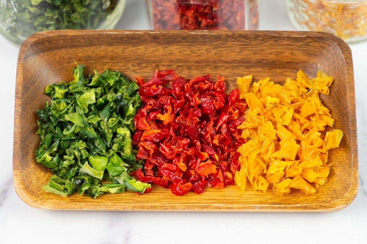 Small piles of green, red, and yellow diced bell peppers on a wooden plate.