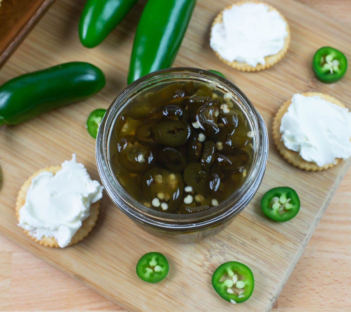 An opened jar of candied jalapeños with crackers and cream cheese.