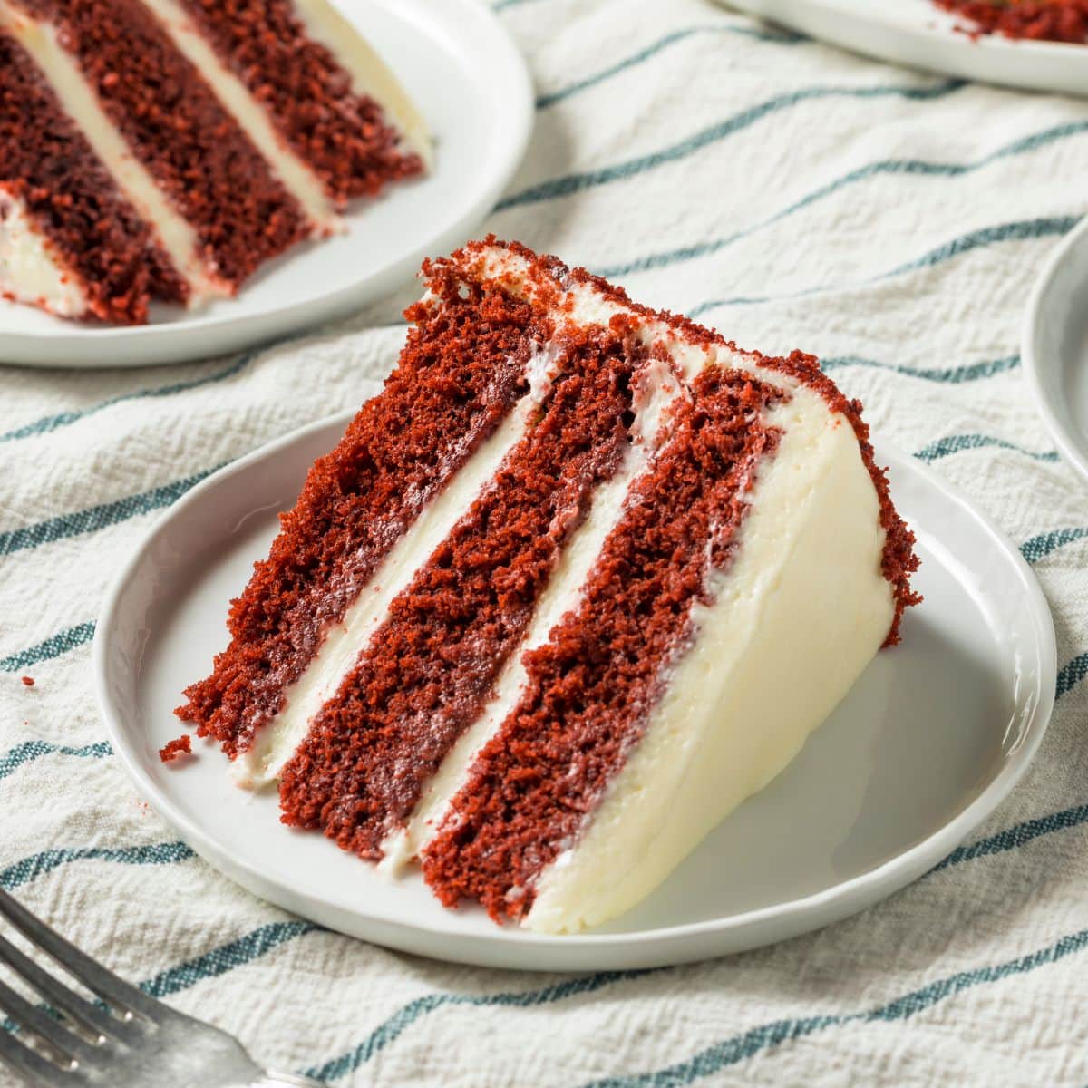 Triple layer red velvet cake slice on a plate.