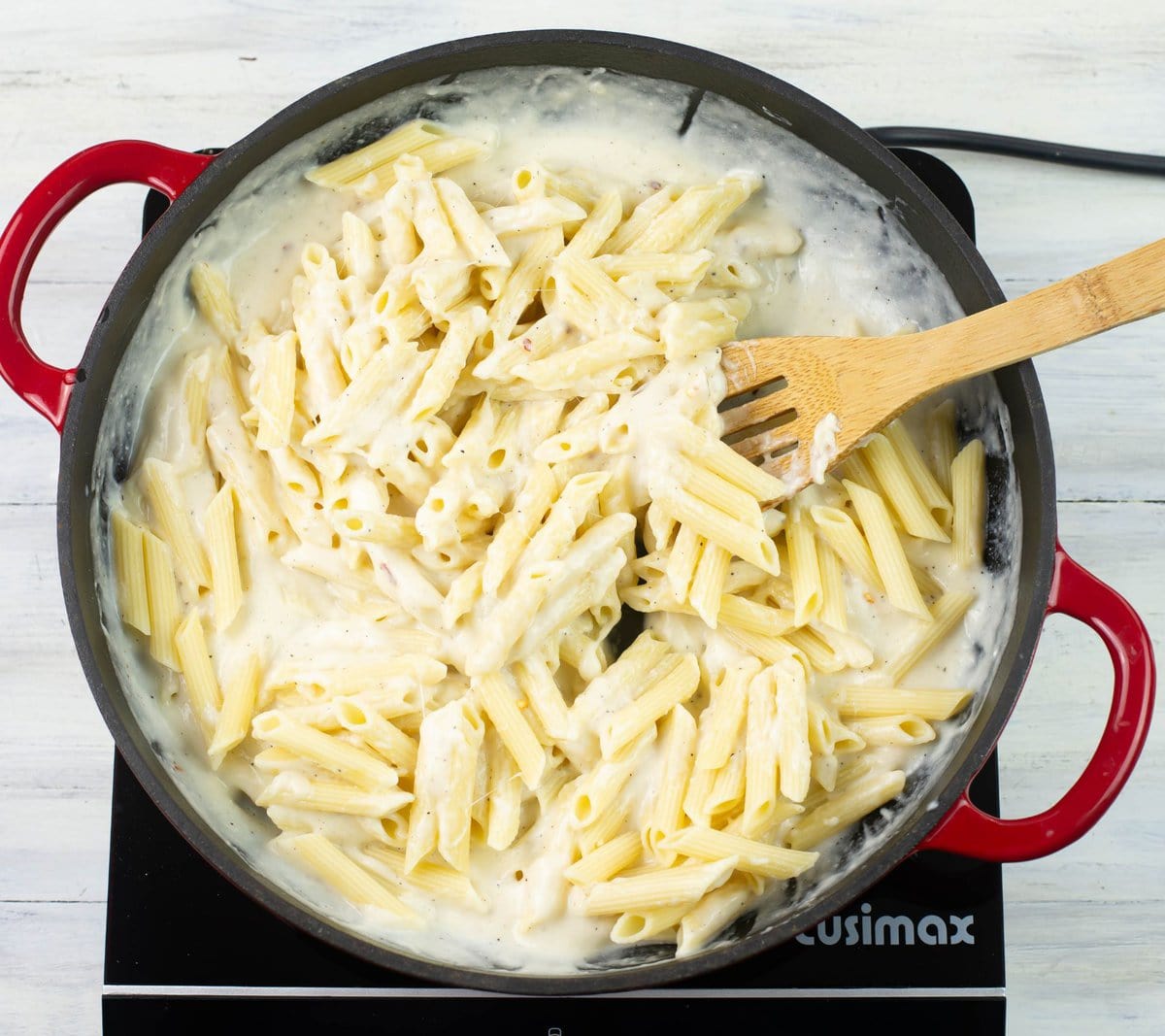 Tossing cooked pasta with alfredo sauce in skillet.