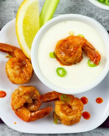 Plump Buffalo Shrimp served on an appetizer plate with a bowl of Garlic Parmesan Dressing.