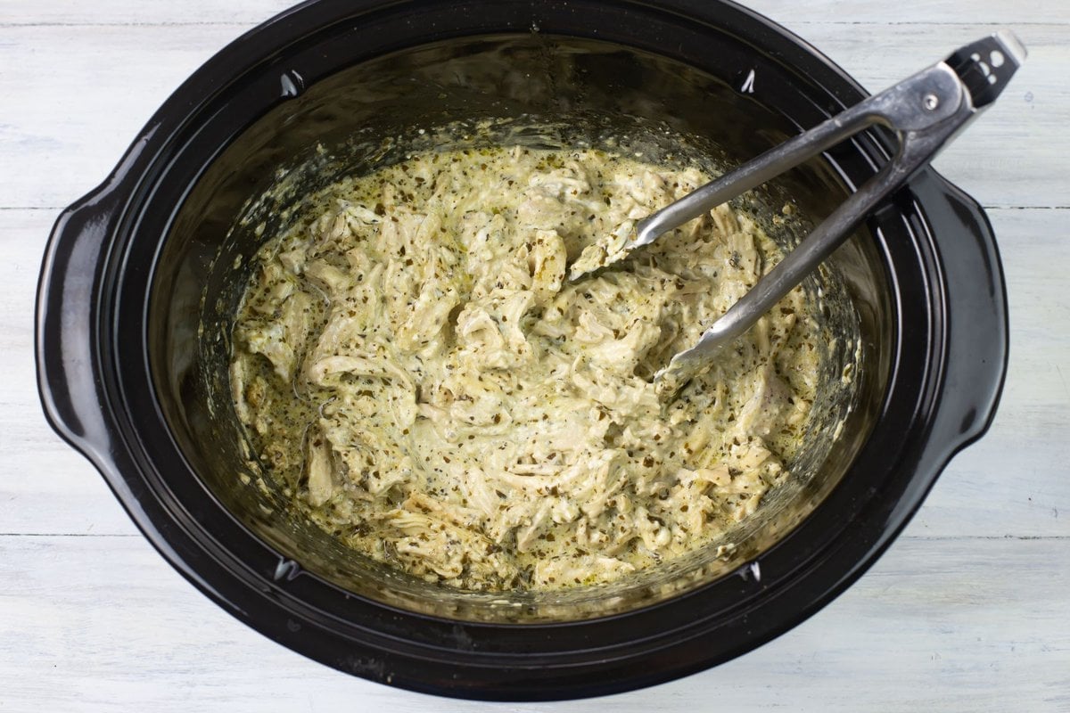 Mixing creamy pesto sauce with shredded chicken.