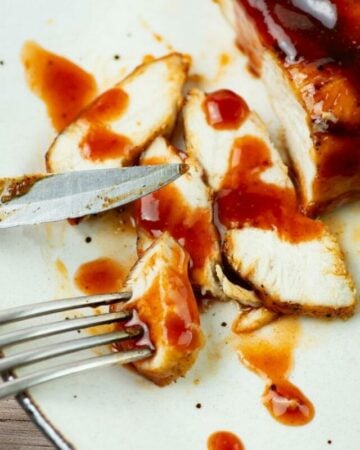 Closeup of a grilled chicken breast cut into slices with honey buffalo bbq sauce drizzled over.