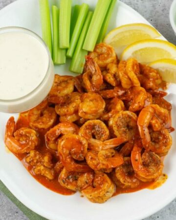 Buffalo Shrimp on a serving platter with celery and creamy Garlic Parmesan Dressing.