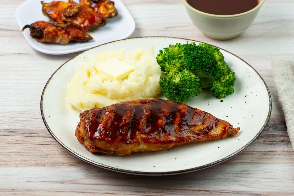 A piece of grilled chicken with honey buffalo bbq sauce on a dinner plate with sides.
