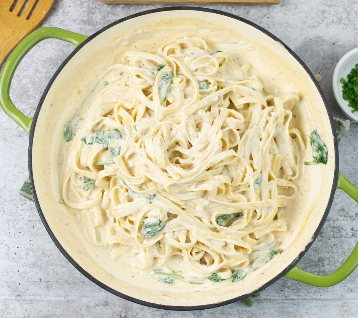 Mixing hot alfredo sauce with fettuccine noodle in a skillet.